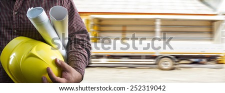 No face Unrecognizable person construction worker man holding in hands blueprint and yellow helmet on empty truck without load with open side walls background Empty copy space for inscription