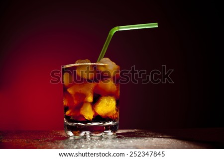 Object of transparent full glass with ice star cubes and sparkling carbonated diet coca coke cola with variety of green plastic tube on red dramatic background Empty Space for inscriptions