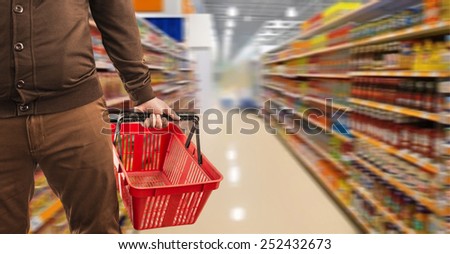 Internet food shop super market  close up hand pushing shopping empty red plastic basket on supermarket shelfs in perspective background Man wear casual brown stylish modern dress