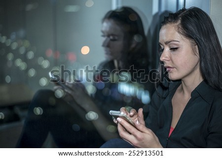 Woman with cell mobile telephone on background of night city. Reflection of face portrait on dark glass and colorful bokeh Light town Cute girl with long brunette hair read e-mail or look image book