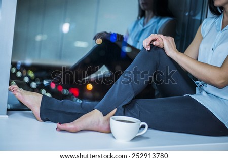 No face Unrecognizable person Romantic Girl With Cup of hot Coffee or black tea near long legs along dark night window View on city town with bokeh light Reflection in glass Hands on knee