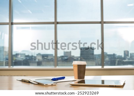 Object tools in office room tablet computer paper cup with hot coffee Cell mobile phone Paper document lie on wooden table against blue sky window with houses Empty space for inscription