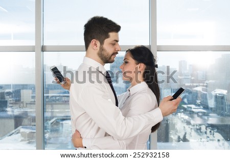on line communication new generation Too busy for caress and romantic love Couple embrace with cell mobile phone in hand against blue sky window background Clerk Man and woman wear white collar shirt
