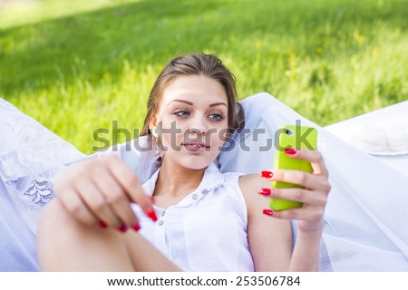 Cute slim girl looking at cell screen read book or watch video on summer fresh green grass background Portrait of Beautiful young adult caucasian woman reading a message on mobile phone
