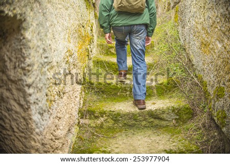 Back view Close up low angle man walking up green grass and moss ancient stones steps Senior wear windcheater with rucksack blue jeans brown leather shoes between wall going up stairway