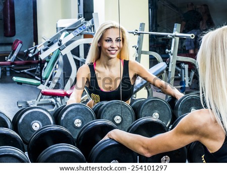close-up shot of the torso of a female dressed in fitness wear, holding a hand weight,facing the camera. Woman look at your self reflection mirror image Arm keep black metal dumbbell
