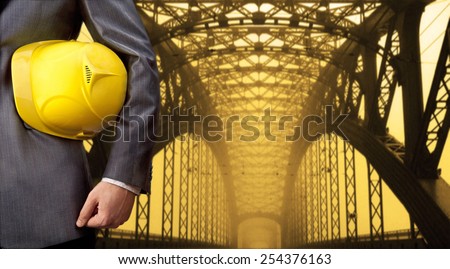 worker or engineer holding in hands yellow helmet for workers security on background of metal bridge over river in perspective buildings idea high way road junctions Empty Copy space for inscription