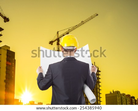 construction worker wearing hard hat.back view worker or engineer with yellow helmet for workers security holding in hands paper plan on the background of a new home dwelling house building