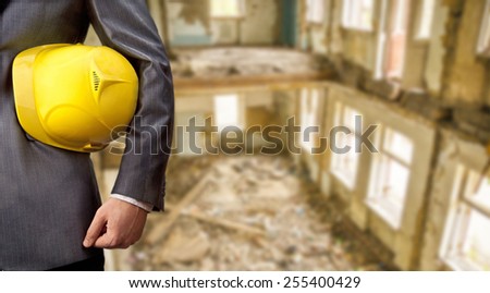 engineer or worker hold in hand yellow plastic helmet for workers security inside against the interior of an old ruined brick building with windows Day light Empty space for inscription