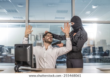 Portrait of woman wear black balaclava hold hair with gun look at hostage scared business man on reflection window background Empty space for inscription Girl sit on table near pc computer Hands up
