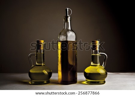 Backdrop of three olive oil glass transparent bottle with cork stand on white table on kitchen space room, on dark black  background Empty space for inscription