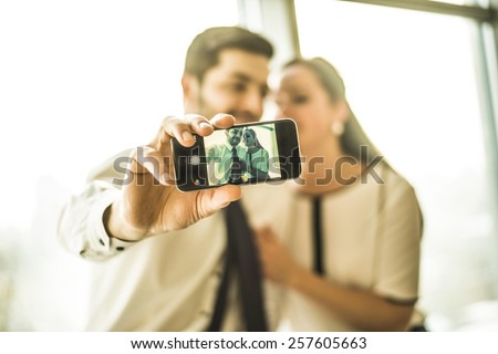 Focus on screen cheerful couple embrace and taking a selfie with a smartphone Man and woman look at mobile phone screen Sun light shine in window glass with plastic frame Empty space for inscription