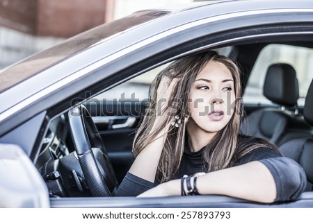 Portrait of female Young brunette dreaming and looking far away girl sitting in luxury black car Slim cute asian scary woman listening music inside black leather chair auto hand Fingers in long hair