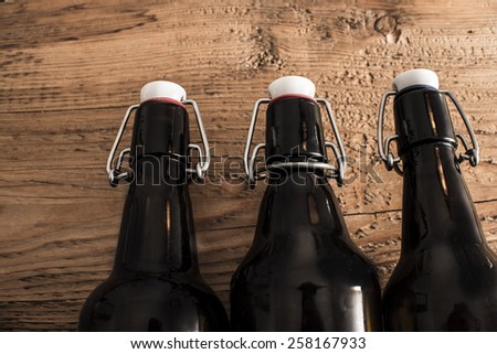 Three full open dark brown Beer Bottle with metal Swing Flip Top Stopper lie on old retro vintage aged texture Wooden Table board Food and drink background Empty Copy Space for inscription