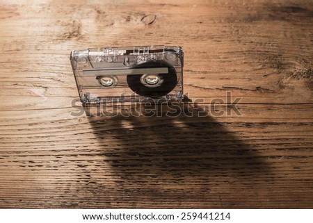 Music concept. Black audio transparent plastic cassette on old aged brown wooden texture background. Vintage, retro style. Shadow from object