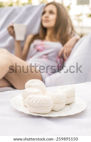 Beautiful girl drink coffee or tea outdoor on green spring park background Young adult woman enjoying and eat unhealthy food snack in lunch break smiling happy.White cakes - zephyr in focus