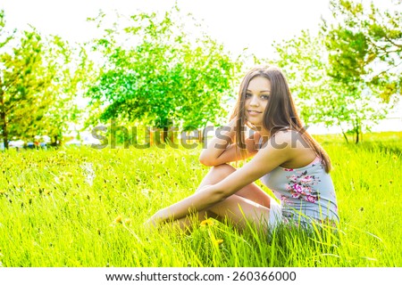 portrait of beautiful young adult woman sit on meadow against white flower on apple tree Cute slim girl in gray dress look at camera and enjoying against summer sky Empty Copy space for inscription
