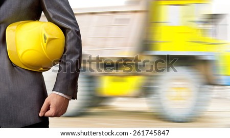 No face Unrecognizable person engineer construction worker hold in hand yellow plastic helmet for workers security against large big truck with load on road Idea concept of logistic transportation