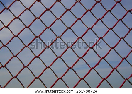 background of Metal mesh fence painting red against blue sky with clouds backdrop Idea of slave and freedom