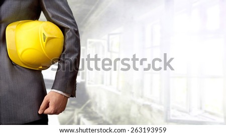 adult engineer or inspector hand holding yellow plastic helmet for workers security over big empty space room with window in perspective and door background No face Copy space for inscription