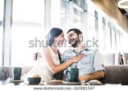 Happy couple enjoy coffee at coffee shop cafe Young adult man and woman kiss touch nose each other against window glass in perspective Romantic relationship Pair embrace and look each other