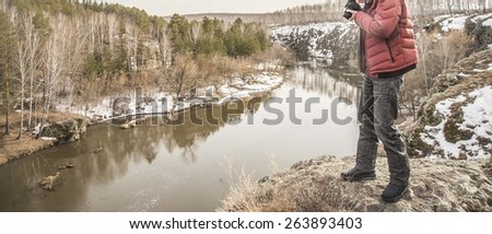 No face Unrecognizable person Caucasian tourist taking photos Man stand near above River between stone mountains Male wear winter warm clothes Red jacket and black jeans