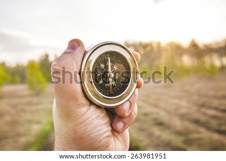 lost man holding compass in middle of forest with many paths to choose from Which direction to go? North or south? Decisions to be made Background of summer or spring meadow or field