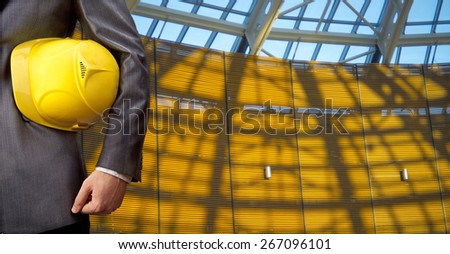 torso engineer or worker hand holding yellow helmet for workers security against blue transparent glass office window and sunset light with shadows background Empty texture space for inscription