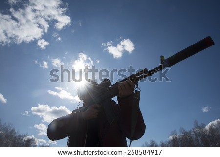 Hunter holding rifle ready to shoot Silhouette Man look at  optical silencer against sun set rays light , blue sky with clouds and trees in forest Aiming at a target outdoor Modern Play laser tag