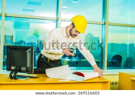 builder man engineer wear yellow security plastic helmet look at blueprint paper construction drawing plan on background of sunset window frame blue yellow sky with clouds near pc monitor computer