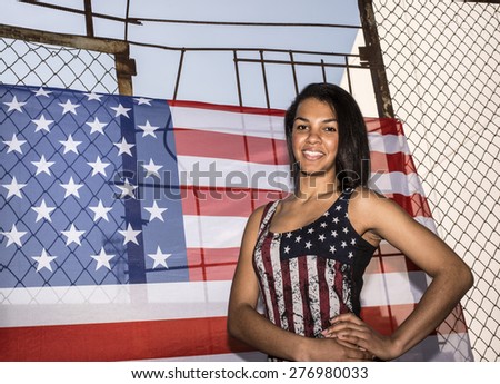 portrait of Beautiful woman, American flag on rusty metal fence. Patriotic concept. All American beauty.Cute young adult girl under  protection of  American flag hang outdoor against blue summer sky