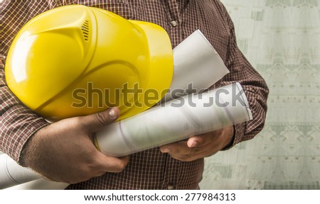 No face Unrecognizable person construction worker man holding in hands blueprint and yellow helmet on green texture wall with wallpaper background Empty copy space for inscription