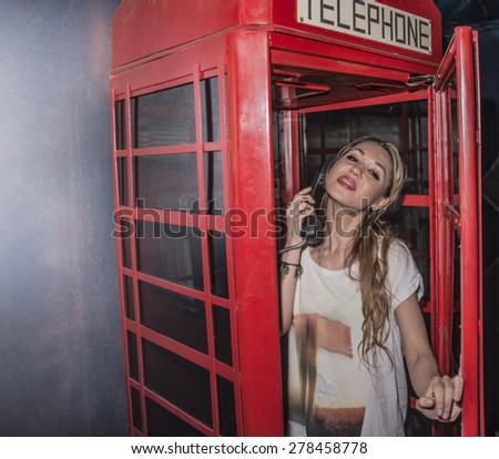 Cute young adult Girl inside a traditional English red telephone booth metal box look at camera Sexy caucasian woman wear stylish white shirt with the handset in hand Female opens the door