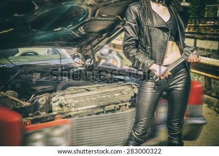No face Unrecognizable person sexy young woman holding metal wrench standing by an open hoof of old retro vintage aged used car Empty space for inscription Idea of repairing auto
