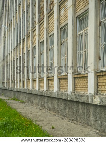 white brick wall of building with barred windows in perspective Fresh spring green grass on floor on background Yellow dandelion Empty outdoor space for object or inscription Vertical format
