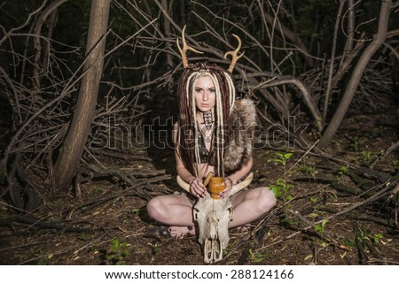 portrait of Beautiful woman with long dreadlocks hair sit near cow skull with horns against wild forest trees Young girl pray satan Woman shaman in ritual garment hold wooden mortar with tamper