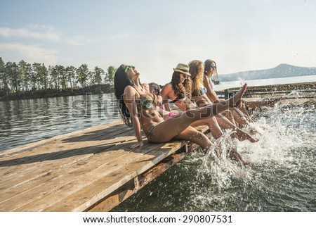 group of happy young woman feet splash water in sea and spraying at the beach on beautiful summer sunset light. Five sexy girls playing on wooden pontoon against blue sky background Enjoy holiday