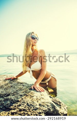 Girl at the sea. Attractive young blond woman in white swimsuit posing at the sea The sexual young blonde girl with a beautiful body sunbathes on a beach in a white bathing suit against  sea