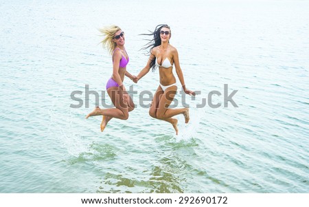 Couple of two woman jump In Water with splash Girls wear sexy bikini Female fly in air under wive texture against forest trees and sky background Empty space for inscription Sunglasses on faces