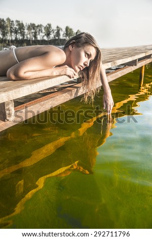 portrait of sad dreaming  beautiful girl lying on wooden and metal pontoon Cute woman thinking about something above water reflection texture against summer forest and blue sky background