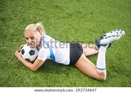 Sexy soccer player lie under ball and wear white and black knee socks Alone woman on green grass field background Full length body of cute blond girl in uniform Empty space for inscription