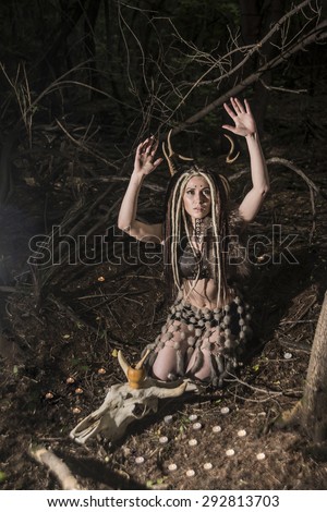 portrait of Beautiful woman with long dreadlocks hair sit near cow skull with horns against wild forest trees Young girl pray satan Woman shaman in ritual garment wear fur and leather clothes
