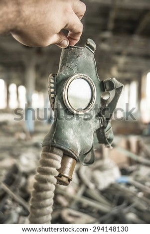 Man holding in hand rubber gas mask against abandoned industrial space with dirty trash Postapokalipsis scene