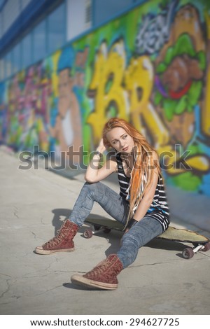 Full length Portrait of Beautiful redhead caucasian teen girl with long skate board stand against graffiti style wall. Outdoors, urban lifestyle. Empty space for inscription. Youth subculture
