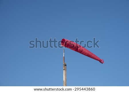 A red wind vane against a blue clear summer sky background  Windsock on wooden stock