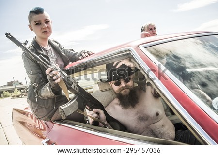 Group of male and female gangsters with guns Man and woman hold Kalashnikov assault rifle and drive inside retro red car on on city street Gangster wear black cowboy hat and circle sunglasses
