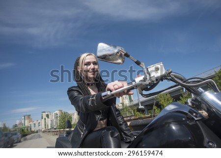 Biker Woman on motorcycle against blue sky with white clouds background Young brutal cute girl sit on chopper and wear black leather jacket and trousers  Empty space for inscription