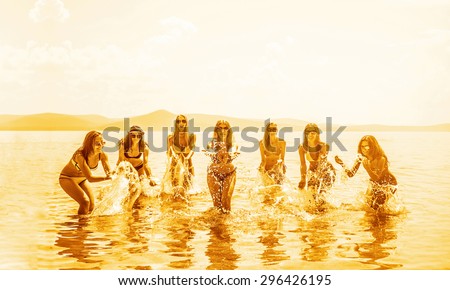 group of happy young people dancing and spraying at the beach on beautiful summer sunset Team of adult girl playing in water against blue sky with clouds and mountain on horizon Hen party