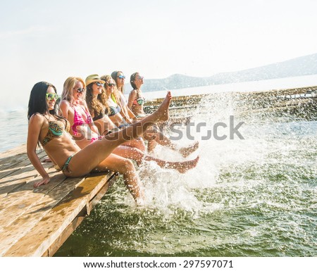 group of happy young woman feet splash water in sea and spraying at the beach on beautiful summer sunset light. Five sexy girls playing on wooden pontoon against blue sky background Enjoy holiday