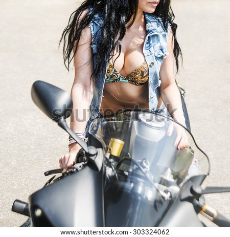 No face Unrecognizable person Beautiful brunette woman sit on black sports motorcycle Very hot sexy young femme fatale girl wear denim vest. Sexy Lady against green summer bush background